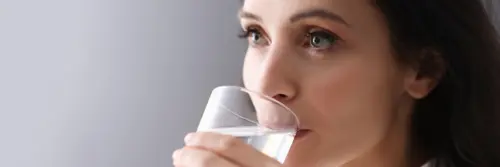 Mlada brineta pije vodu iz čaše kako bi ostala hidrirana.