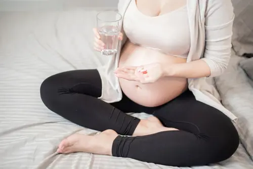 Trudnica sjedi na krevetu i uzima svoju dnevnu dozu vitamina.